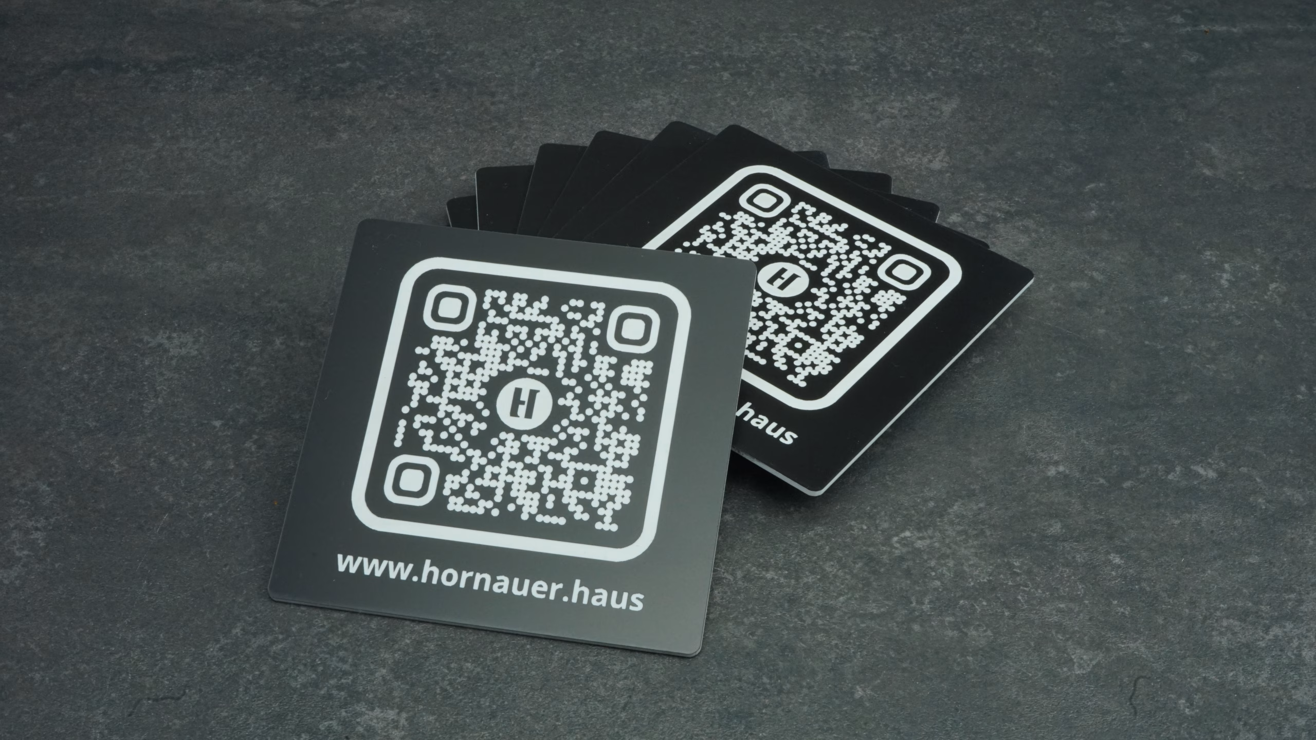 Schwarze Kunststoffschilder mit weißem QR Code und Webadresse auf dunklen Untergrund.