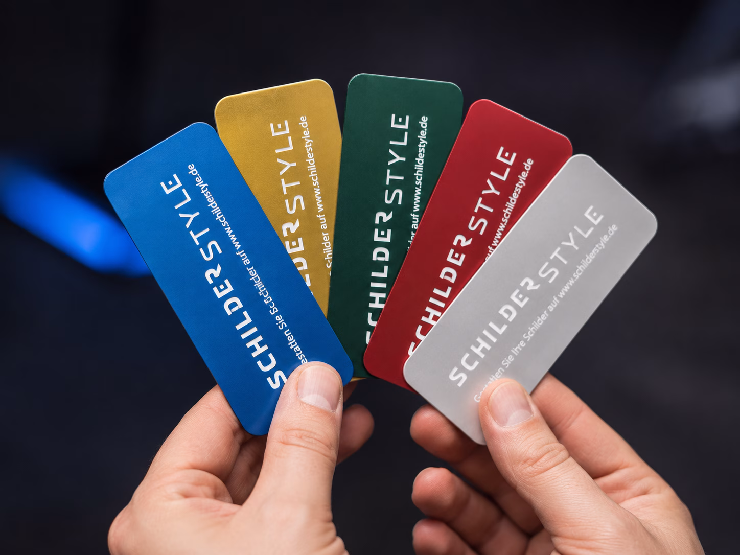 Farbige Aluminiumschilder in Blau, Gold, Rot und Silber werden in einer Hand präsentiert.